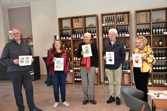 Fünf Weinfreunde stehen in der Vinothek des Weingutes Paulinenhof und halten lustige Comiczeichnungen von „Hefemännchen“ vor sich.