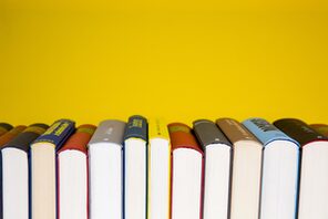 gestapelte Bücher nebeneinander, gelber Hintergrund © Pixabay