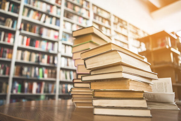 Ein Bücherstapel vor einem Bücherregal © AdobeStock Yakobchuk Olena